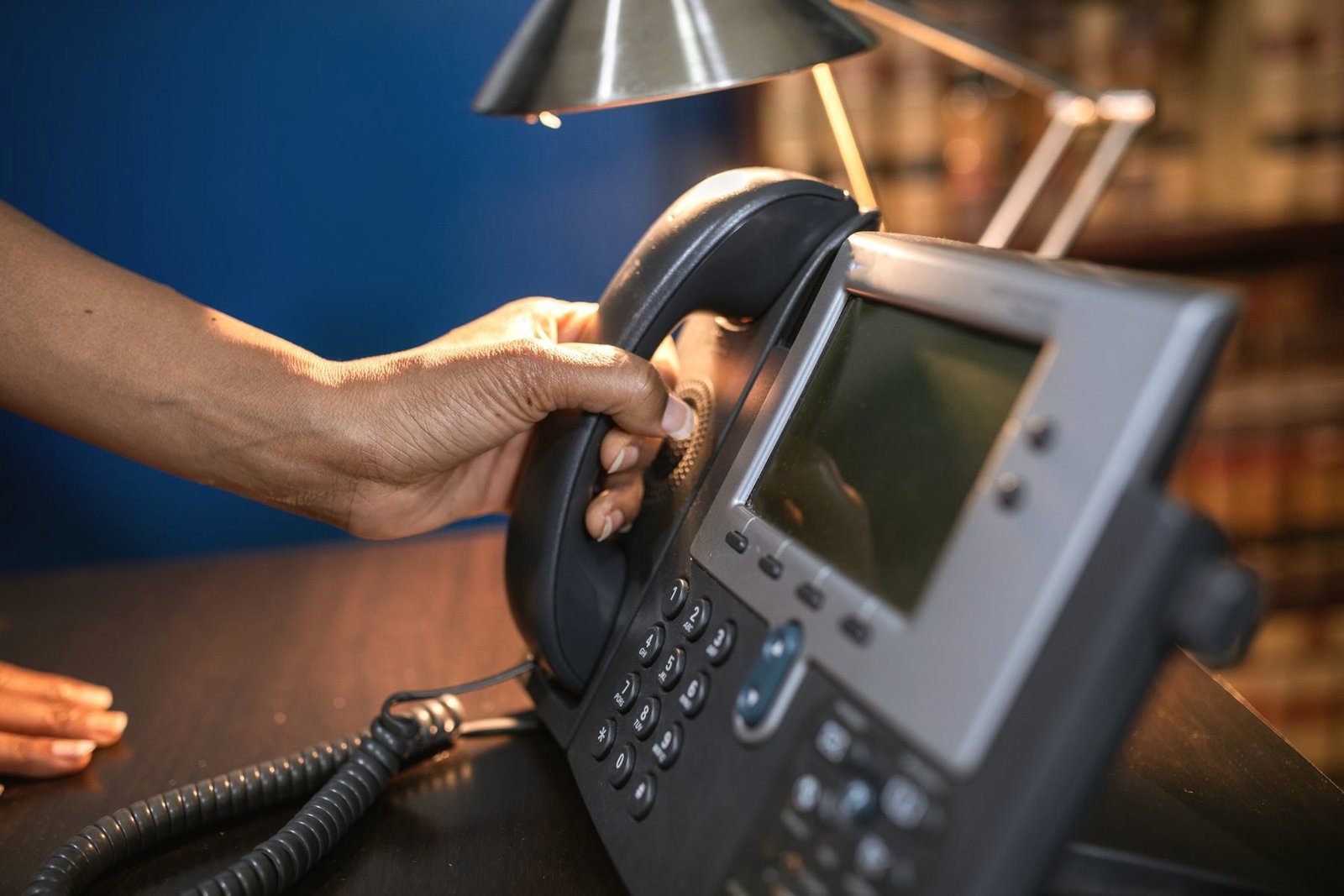 A hand lifting a telephone handset from a desk phone.